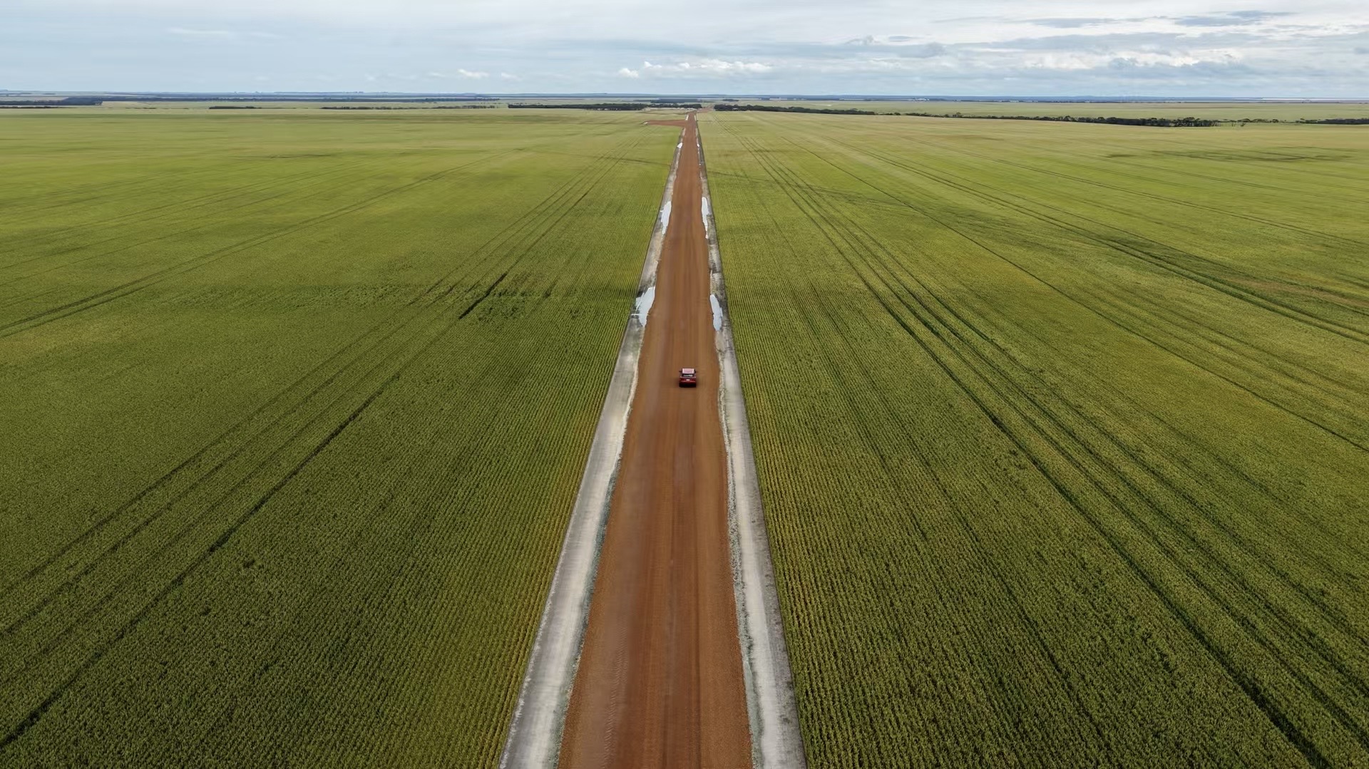 A red car on a country road between green fields, photographed from above during the trip.